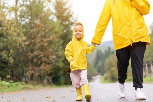 Rainy day Mother and little daughter walking after rain dressed yellow raincoat Happy family with one child. Positive emotions