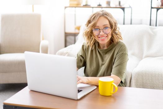 Woman with glasses use laptop drink morning coffee sitting floor near sofa big window background home interior Freelance female working home Distance learning student relaxing watch video lessons.