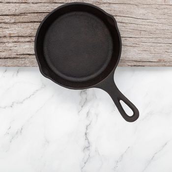 Empty old cast iron skillet set up on white marble  background with flat lay and copy space.