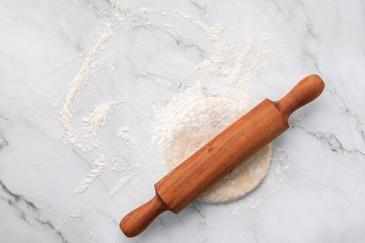 Scattered wheat flour and fresh homemade yeast dough kneaded on marble table with rolling pin on marble table flat lay.