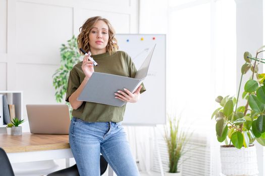 Businesswoman holding folder for paper write marker thinking dreaming standing near office table. Business person femal ypoung adult caucasian on modern white interior