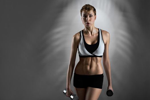 Healthy lifestyle. Horizontal portrait of a beautiful young sporty woman sweating after exercising with weights looking away on grey background copyspace 