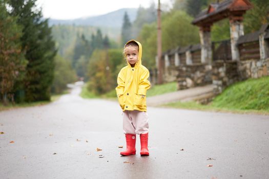 Playful girl wearing yellow raincoat while jumping in puddle during rainfall Happy childhood