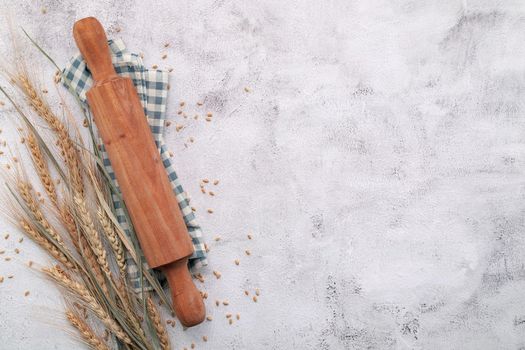 Wheat ears and wheat grains setup with rolling pin on white concrete background.