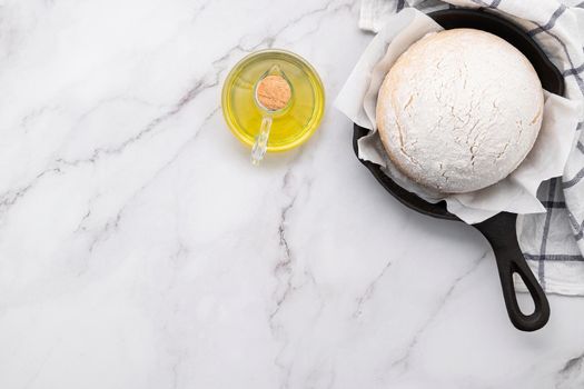 Fresh raw  homemade yeast dough resting in cast iron skillet on marble table flat lay.