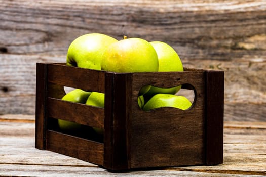 Wooden crate with ripe green apples on wooden table.