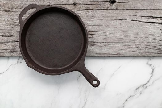 Empty old cast iron skillet set up on white marble  background with flat lay and copy space.