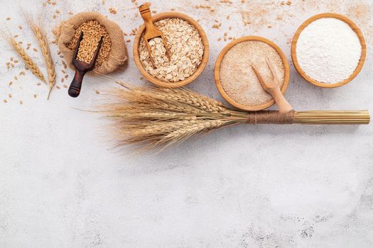 Wheat grains , brown wheat flour and white wheat flour in wooden bowl set up on white concrete background.