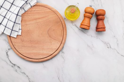 Empty wooden pizza platter with napkin  set up on marble stone kitchen table. Pizza board and tablecloth on white marble background.