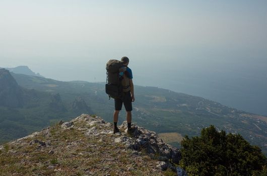 A tourist with a large backpack admires the landscape, standing on the edge of the abyss.