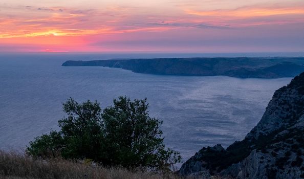 The sun setting into the sea and the long cape crashing into the Black Sea at sunset. Coast of the Crimean Peninsula near Balaklava.