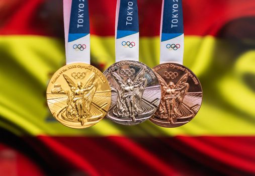 April 25, 2021 Tokyo, Japan. Gold, silver and bronze medals of the XXXII Summer Olympic Games 2020 in Tokyo on the background of the flag of Spain.