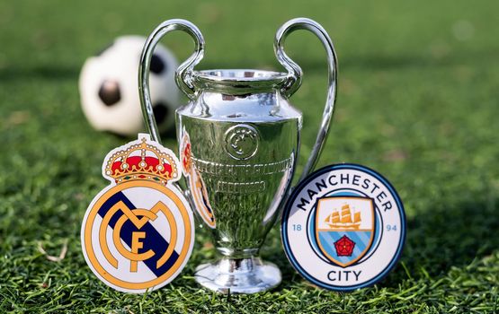 April 16, 2021 Moscow, Russia. The UEFA Champions League Cup and the emblems of the football clubs Manchester City F. C. and Real Madrid CF on the green grass of the lawn.