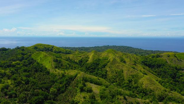 Hills and mountains covered with green grass against a background of blue sky and clouds. Bohol, Philippines. Summer landscape.
