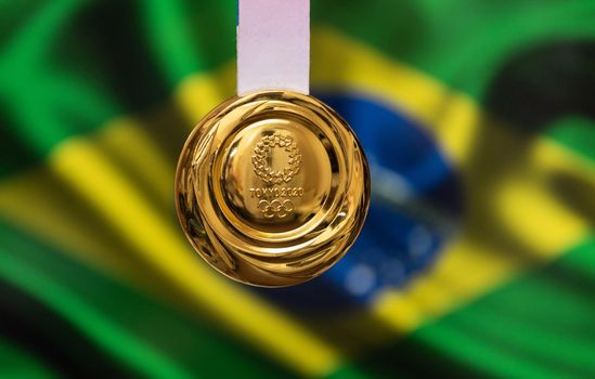 April 25, 2021 Tokyo, Japan. Gold medal of the XXXII Summer Olympic Games 2020 in Tokyo on the background of the flag of Brazil.