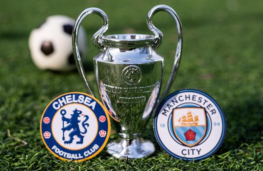 April 16, 2021 Moscow, Russia. The UEFA Champions League Cup and the emblems of the Manchester City F. C. and Chelsea F. C. London football clubs on the green grass of the lawn.