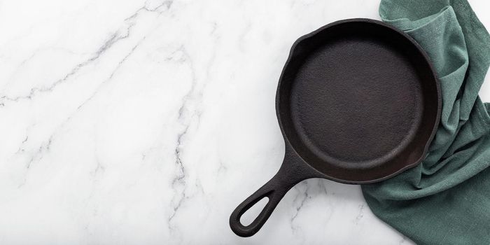 Empty old cast iron skillet set up on white marble  background with flat lay and copy space.