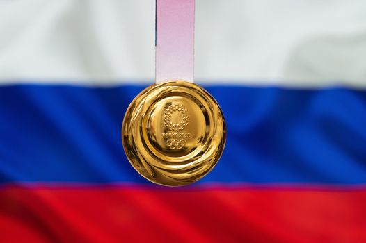 April 25, 2021 Tokyo, Japan. Gold medal of the XXXII Summer Olympic Games 2020 in Tokyo on the background of the flag of Russia.