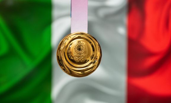 April 25, 2021 Tokyo, Japan. Gold medal of the XXXII Summer Olympic Games 2020 in Tokyo on the background of the flag of Italy.