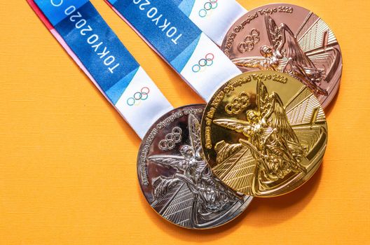 April 25, 2021 Tokyo, Japan. Gold, silver and bronze medals of the XXXII Summer Olympic Games in Tokyo on a yellow background.