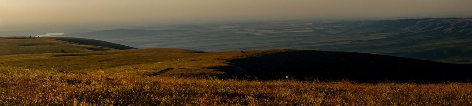 Pid to the surrounding mountains from the lower plateau of Chatyr-Dag in Crimea in the light of the setting sun. Panorama