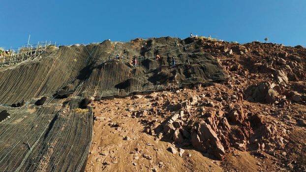 Workers strengthen the slope of the mountain with metal mesh preventing rockfall and landslide on the road, above view. workers constructing anti-landslide concrete wall prevent protect against rock slides. safety concept