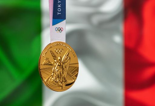 April 25, 2021 Tokyo, Japan. Gold medal of the XXXII Summer Olympic Games 2020 in Tokyo on the background of the flag of Italy.