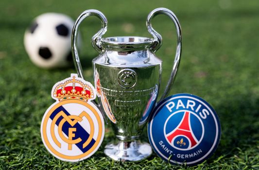 April 16, 2021 Moscow, Russia. The UEFA Champions League Cup and the emblems of the football clubs Paris Saint-Germain F. C. and Real Madrid CF on the green grass of the lawn.