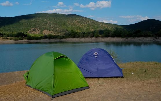 Multicolored tents on the shore of a mountain lake against the backdrop of inaccessible rocks surrounded by a green forest.