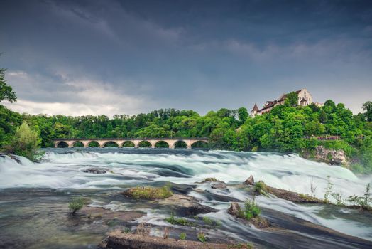 Natural Scenery of Rhine Falls and Swiss Church Culture at Schaffhausen City, Switzerland. Beautiful Nature Waterfront View of Rhine River With Architecture Historical Church Building in Summer. 