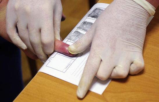 A police officer wearing rubber gloves takes a fingerprint of a suspect.