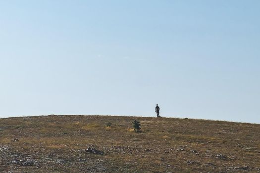 Silhouette of a young man running to the top of a high hill on a clear sunny day.