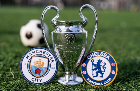 April 16, 2021 Moscow, Russia. The UEFA Champions League Cup and the emblems of the Manchester City F. C. and Chelsea F. C. London football clubs on the green grass of the lawn.