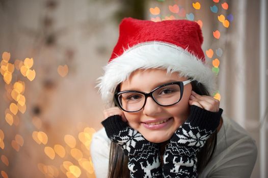 Good little girl. Closeup portrait of a cute cheerful girl relaxing at home on Christmas eve smiling cupping her face wearing Santa Claus hat copyspace soft focus and noise. 2018, 2019