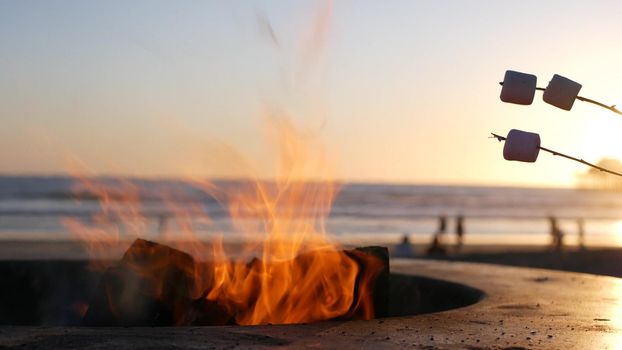 Campfire pit by Oceanside pier, California USA. Camp fire on ocean beach, bonfire flame in cement ring place for bbq, sea water waves. Heating, roast or toast marshmallow on stick. Romantic sunset sky