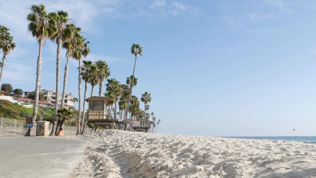 Tropical palm trees, white sandy beach by sea water wave, pacific ocean coast, San Clemente California USA. Blue sky and lifeguard tower. Life guard watchtower hut, summertime shore. Los Angeles vibes