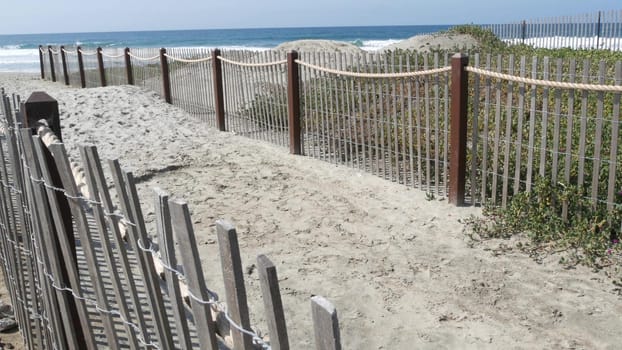 Pacific ocean coast, greenery and wooden picket fence on sea shore. Blue water waves on sunny summer beach, Encinitas shoreline, California USA. Coastline near Los Angeles. Coastal access entrance.