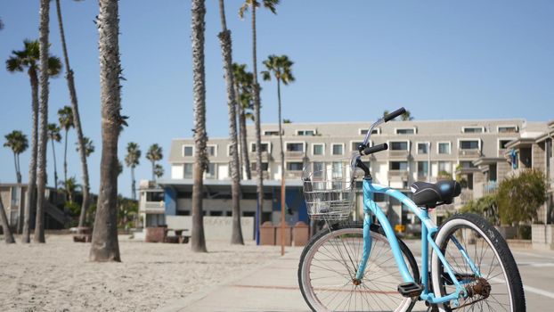 Blue bicycle, cruiser bike by ocean beach, pacific coast, Oceanside California USA. Summertime vacations, sea shore. Vintage cycle by beachfront houses, waterfront lodging. Buildings and palm trees.