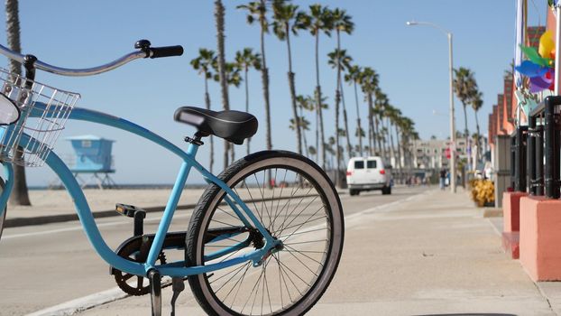 Blue bicycle, cruiser bike by ocean beach, pacific coast, Oceanside California USA. Summertime vacations, sea shore. Vintage cycle by beachfront house, waterfront cotteges, bungalow huts and palm tree