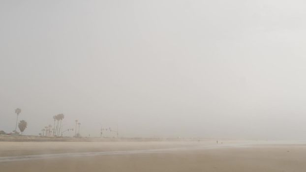 Sandy misty beach, Encinitas California USA. Pacific ocean coast, dense fog brume, empty sea shore. Coastline near Los Angeles, milky smog haze. Gloomy weather on shoreline. Cloudy grey monochrome sky