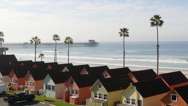 Colorful waterfront cottages in Oceanside, California USA. Multicolor bungalow huts by sea, beachfront lodging. Many vacation houses on beach, ocean waves and palm trees. Summer seascape on sunny day.