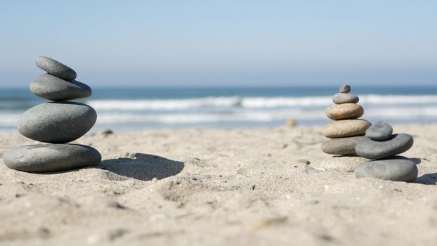 Rock balancing on ocean beach, stones stacking by sea water waves. Pyramid of pebbles on sandy shore. Stable pile or heap in soft focus with bokeh, close up. Zen balance, minimalism, harmony and peace