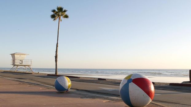 Pacific ocean beach, Oceanside California USA. Ball, lifeguard tower, life guard watchtower hut and tropical palm tree, sky, beachfront street, waterfront road. Los Angeles vibes, aesthetic atmosphere