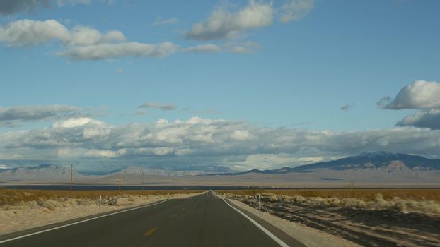 Road trip, driving auto from Death Valley to Las Vegas, Nevada USA. Hitchhiking traveling in America. Highway journey, dramatic atmosphere, clouds, mountain and Mojave desert wilderness. View from car