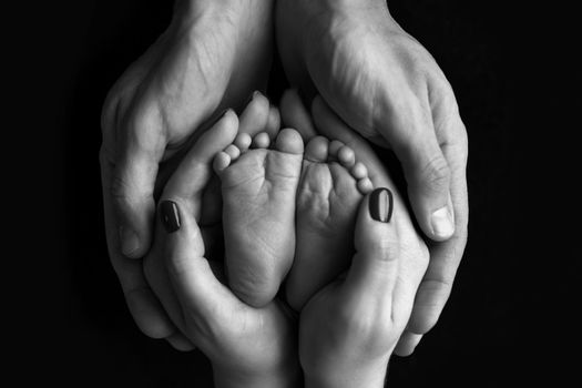 Children's feet in hold hands of mother and father on white. Mother, father and newborn Child. Happy Family people concept. Black and white. High quality photo