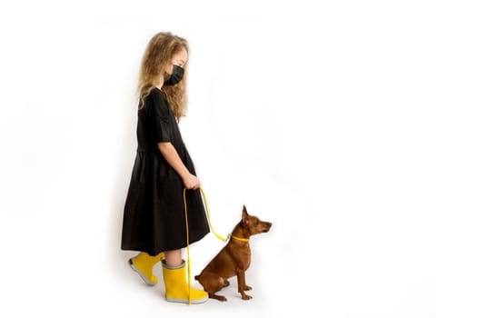 A girl in a black protective antiviral mask walks the dog. High quality photo