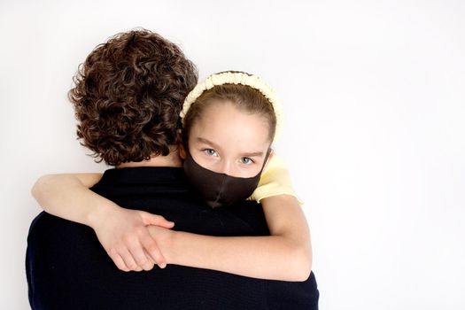 A teenage girl in a black antibacterial mask and a yellow T-shirt in her father's arms.