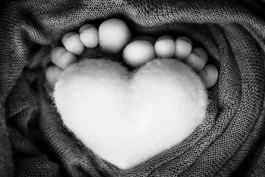 Feet of a newborn with a woolen heart, wrapped in a soft blanket. Black and white studio photography. High quality photo