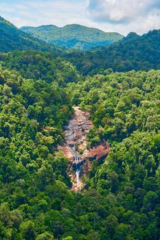 A majestic waterfall flows down the cliff in the dense jungle.