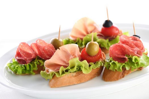 Tender baguette canapes with Leaf lettuce, salami or Parma ham, tomatoes, mozzarella and olive. Delicacy assorted platter for at the party.
